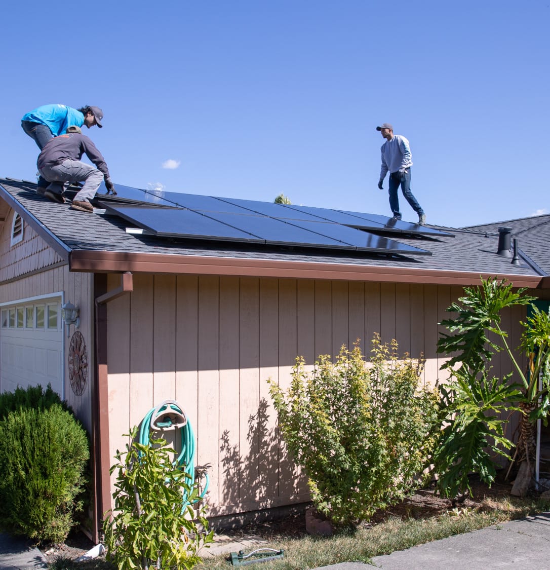 Three men installing solar panels onto the roof of a house