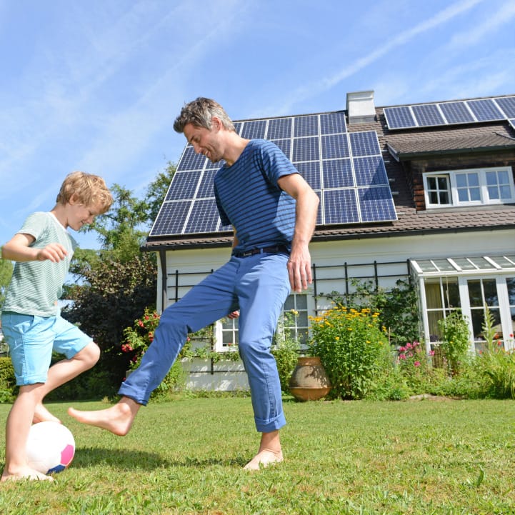 Father and son playing soccer in the yard of a solar panel-roofed house