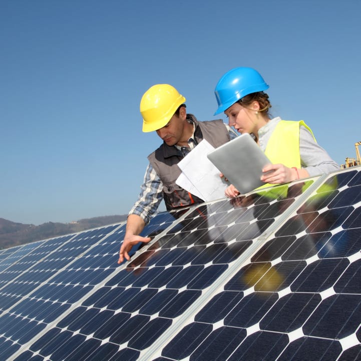 Two crew members in hard hats holding notes and inspecting a solar panel