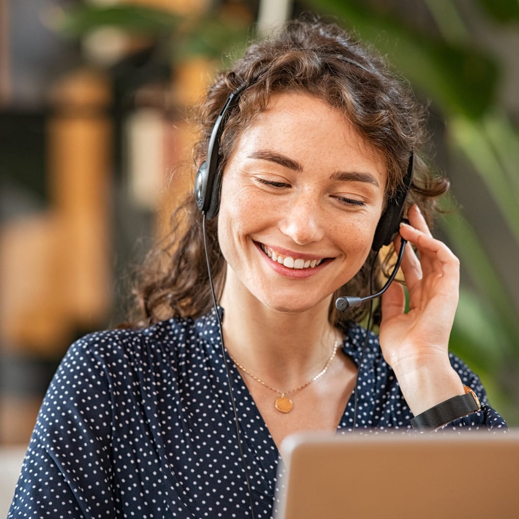 Smiling woman sitting at a computer wearing headphones with attached microphone