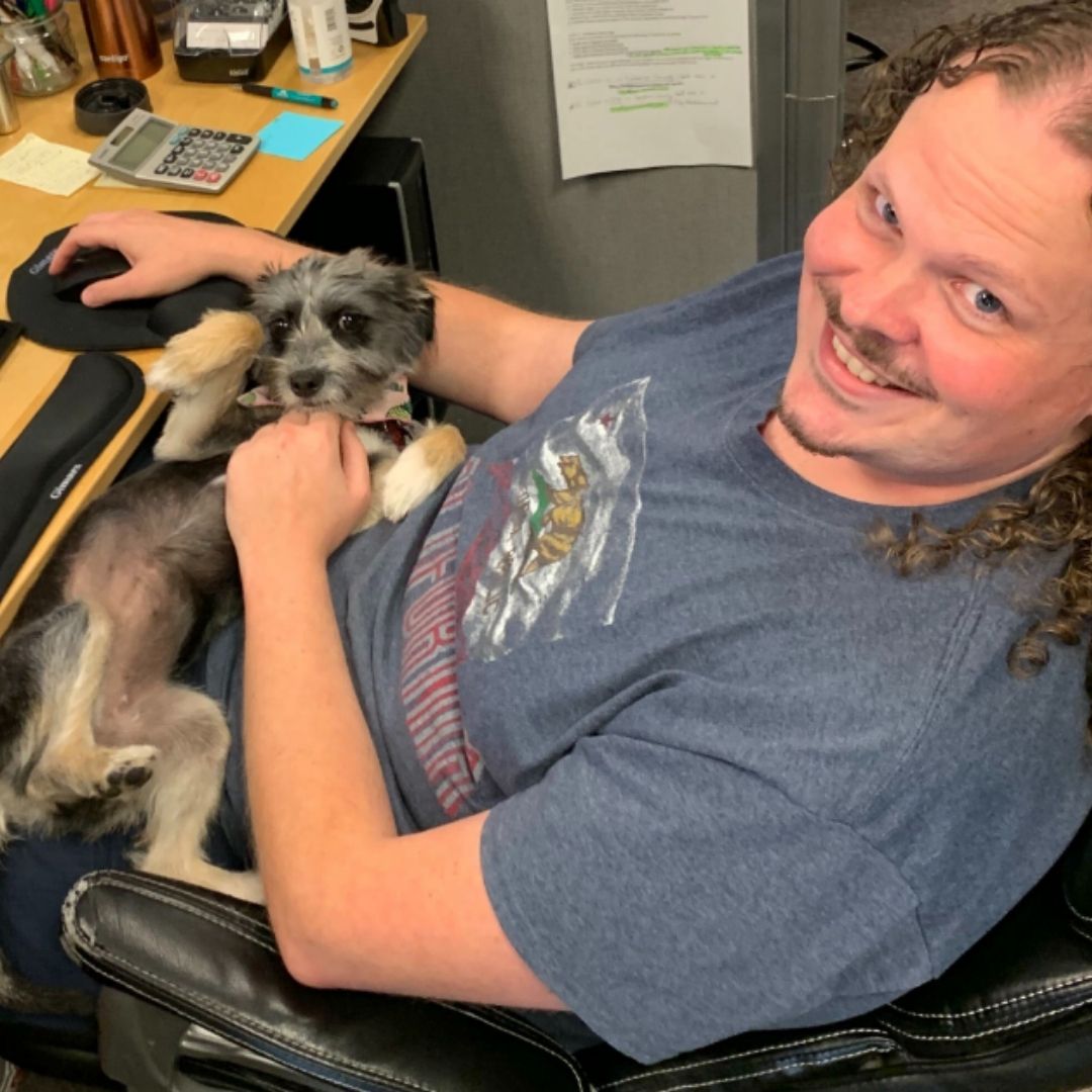 Simply Solar employee Matt Robertson, Operations Specialist, sitting at desk with a dog in his lap